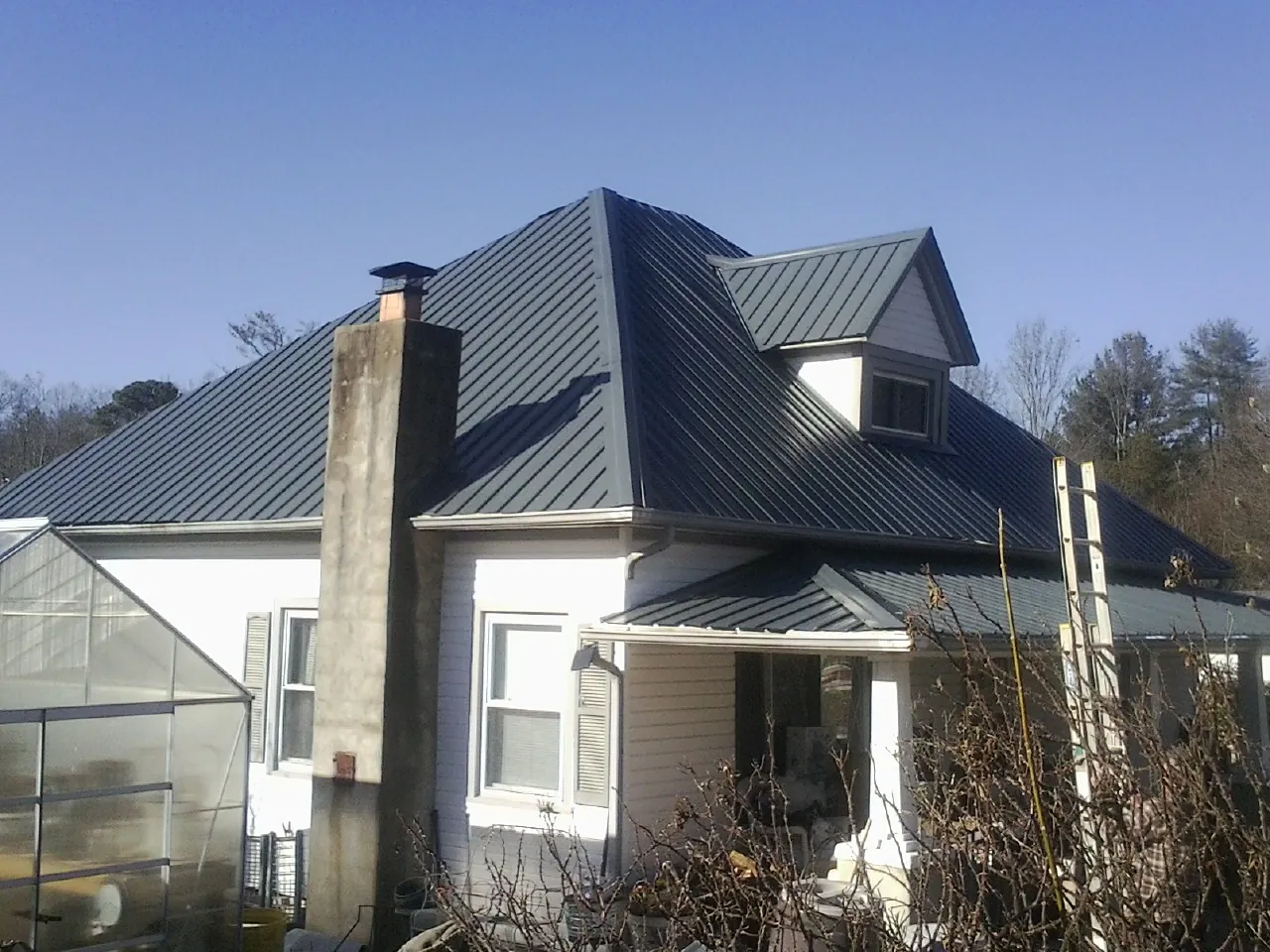 Dark blue standing seam metal roof on a white farmhouse with dormer — Slate & Tile Roof Repair by Roofing Brothers in Custer