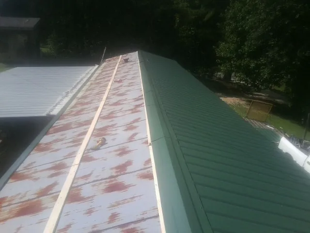 Old rusted panels beside newly installed green metal roofing — Wind Damage Roof Repair by Roofing Brothers in Custer